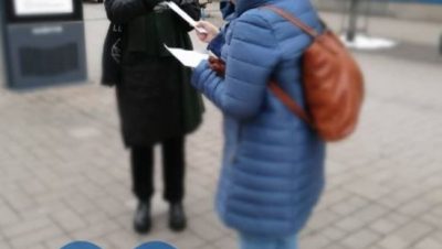 nainen ojentaa postikorttia toiselle naiselle kadulla