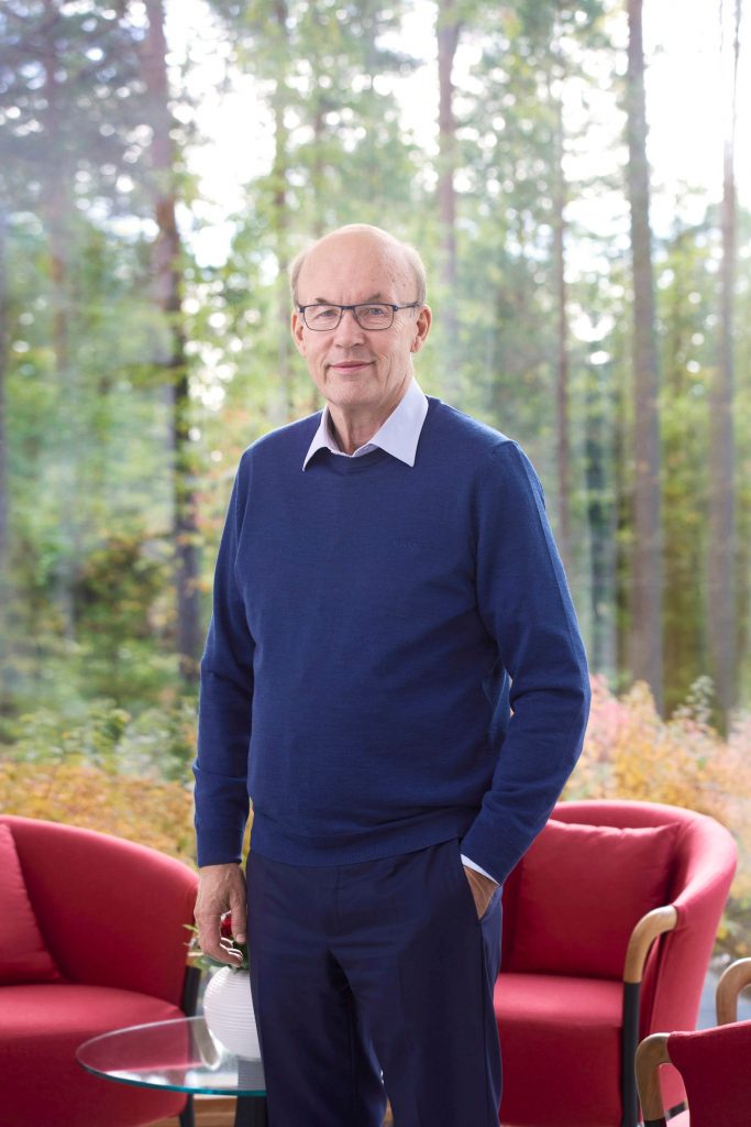 Matti Alahuhta seisoo kotonaan ikkunan edessä. Takana näkyy metsämaisema.