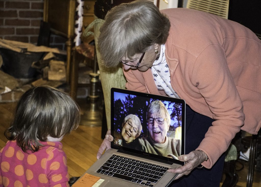 Vanha nainen näyttää tietokoneelta pienelle tytölle kuvaa kahdesta muusta vanhasta henkilöstä. 