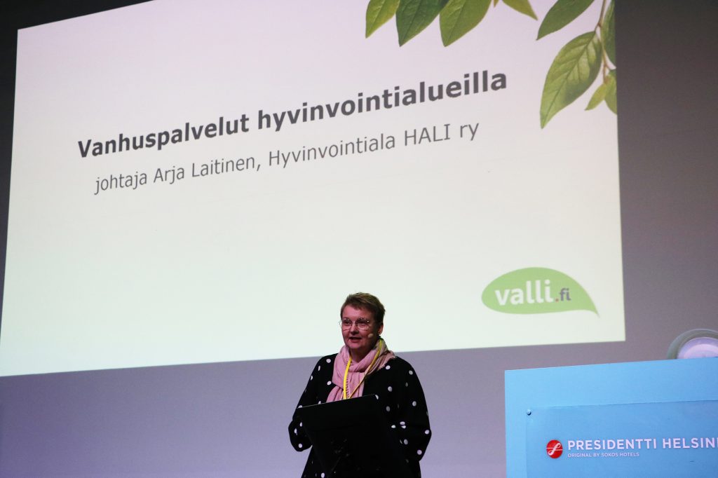 Arja Laitinen puhumassa seminaarissa, taustalla heijastettuna hänen esityksensä otsikko Vanhuspalvelut hyvinvointialueilla.