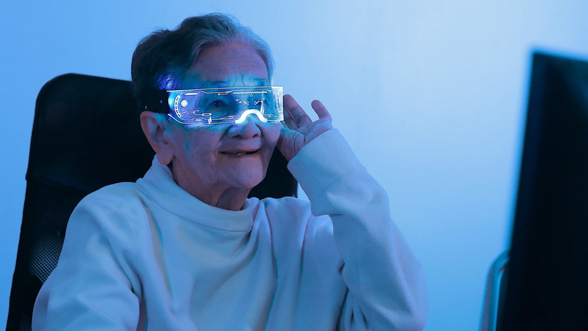 Vanha nainen katsoo hymyilleen tietokoneen näyttöä. Päässään hänellä on älylasit.