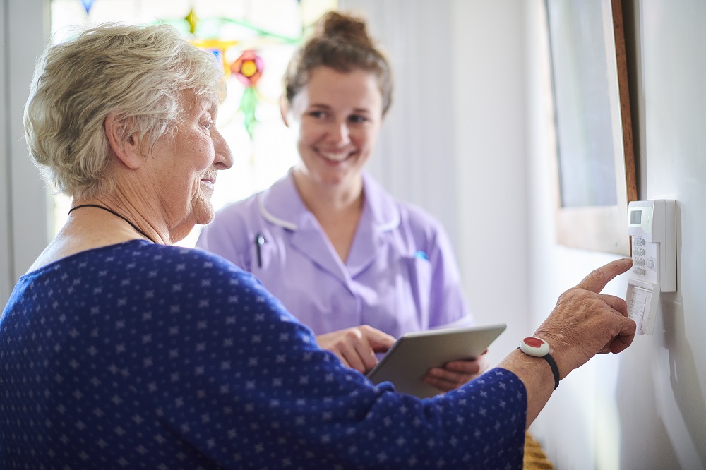 home carer showing senior woman her alarm panel Vanha ja nuorempi henkilö kokeilevat yhdessä kodin turvajärjestelmää.