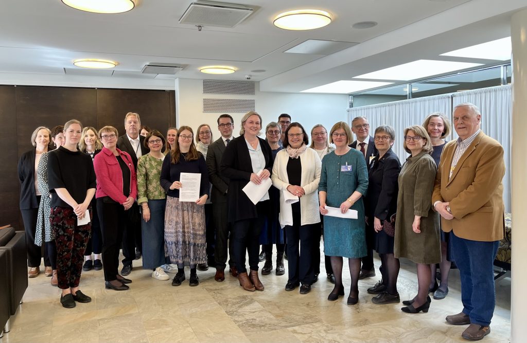 Suuri joukko ihmisiä poseeraa ryhmäkuvassa eduskunnan tiloissa.
