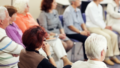 Ryhmä eri ikäisiä ihmisiä kuuntelee ja katsoo samaan suuntaan.